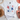 White t-shirt with red, blue, and white stars and text on a light surface with shoes and decorative items.
