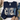 A navy blue sweatshirt laid flat on a white wood surface, featuring the word "COZY" in large decorative letters with plaid, polka dot, snowflake, and snowman motifs. Jeans, a hat, eucalyptus leaves, and tan shoes are styled around it.