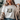 Woman wearing a white t-shirt with 'Jesus was all along' design.