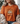 Person wearing an orange t-shirt with a floral and pumpkin design, sitting on a couch.