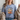 Woman wearing a blue t-shirt with a floral and pumpkin design, sitting on a couch.