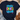 Navy blue t-shirt with colorful 'Sprinkle Kindness Everywhere' text on a textured surface.
