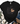 A black short-sleeve T-shirt laid flat with a leopard-print apple graphic and a tan heart shape on the front. The shirt is styled in a flat-lay arrangement with blue jeans, brown shoes, a cream throw blanket, and greenery on a white wood background.