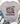 A light gray graphic t-shirt with a colorful retro smiley face design and the text 'Be happy it drives people crazy', styled in a flat lay with jeans, white sneakers, a straw hat, and eucalyptus on a white wood background.