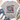 A light gray graphic t-shirt with a colorful retro smiley face design and the text 'Be happy it drives people crazy', styled in a flat lay with jeans, white sneakers, a straw hat, and eucalyptus on a white wood background.
