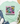 A mint green graphic t-shirt with a distressed smiley face design and the text 'Be happy It drives people crazy', styled in a flat lay with blue jeans, white sneakers, a straw hat, and eucalyptus on a white wood background.