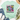 A mint green graphic t-shirt with a distressed smiley face design and the text 'Be happy It drives people crazy', styled in a flat lay with blue jeans, white sneakers, a straw hat, and eucalyptus on a white wood background.