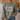 A person wearing an olive green crewneck sweatshirt with a graphic that reads 'but GOD' in white and brown camouflage print, paired with blue jeans in a cozy indoor setting.