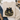 A folded beige sweatshirt laid flat on a white wood surface, featuring a graphic of a pumpkin with a green camouflage pattern, black bow, and gold outline. Surrounding props include blue jeans, a brown shoe, a plaid scarf, and a cup of coffee.