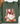 An olive green crewneck sweatshirt featuring a festive Christmas graphic of a white goose with a red bow, surrounded by pink flowers, candy canes, ornaments, and gifts. The sweatshirt is styled flat on a white marble surface with a brown hat and dried flowers as props.