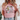 A woman wearing a light pink graphic T-shirt with a floral and cross design that reads 'Daughter of the King' in black text. She is also wearing light blue jeans and a cream knit cardigan, with blonde hair and a leafy plant visible in the background.