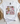 A white short-sleeve T-shirt laid flat on a light surface, styled with a decorative graphic that reads 'Daughter of the King' with a cross, flowers, leopard print, and pastel accents. The shirt is surrounded by props including a woven basket, wooden beads, a paper fan, and pointed flats.