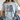 A woman wearing a light blue graphic t-shirt with a cartoon owl and the text 'DOING MY BEST LETTING GOD DO THE REST'.