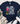 A navy blue graphic t-shirt laid flat on a light wood background, styled with a cream throw blanket, greenery, blue jeans, and white sneakers. The t-shirt features a colorful cartoon owl and the text 'DOING MY BEST LETTING GOD DO THE REST'.