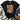 A black short-sleeve graphic T-shirt laid flat on a white wood background, styled with a cream throw blanket, greenery, blue jeans, and brown lace-up boots. The shirt features a colorful patchwork-style 'LOVE LIKE DOLLY' text design with butterflies and leopard print details.