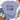A lavender short-sleeve graphic T-shirt laid flat on a white wood background, styled with jeans, beige loafers, a straw hat, and eucalyptus stems. The shirt has a colorful floral 'FAITH' word graphic with small hearts and the words 'OVER FEAR' in black script.