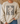 A person wearing a cream-colored crewneck sweatshirt with a graphic print that reads 'FAITH FAITH FAITH' in distressed black letters, overlaid with a gift box design featuring a beige polka-dot ribbon. The person is also wearing blue jeans, standing in a cozy indoor setting with a couch and dried palm leaves in the background.