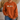 A person wearing a rust-orange crewneck sweatshirt with a graphic of four marshmallows walking, paired with blue jeans in a cozy indoor setting.