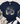 A navy blue graphic t-shirt with a western-themed design reading 'find Joy in the little things' with a dandelion, cowboy boots, cactus, and hat. The shirt is styled in a flat lay with distressed blue jeans, white sneakers, a fringed throw blanket, and greenery on a white wood background.