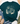 A dark teal graphic t-shirt styled in a flat lay with blue jeans, beige loafers, a straw hat, and eucalyptus on a white wood background. The t-shirt features a cream-colored graphic with the text 'find joy in the little things' surrounded by a dandelion, cacti, cowboy boots, and a cowboy hat.