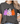 A woman wearing a dark gray heather t-shirt with a graphic of three cute Halloween ghosts in purple checkerboard, white with orange butterflies, and orange with pink spots, paired with blue jeans.