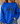 A woman wearing a bright royal blue crewneck sweatshirt with a dark graphic text print reading 'HIGHWAY JESUS TO HEAVEN' across the chest, paired with blue jeans in a cozy indoor setting.
