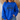 A woman wearing a bright royal blue crewneck sweatshirt with a dark graphic text print reading 'HIGHWAY JESUS TO HEAVEN' across the chest, paired with blue jeans in a cozy indoor setting.