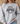A woman wearing a light heather gray crewneck sweatshirt with a black graphic print that reads 'HIGHWAY JESUS TO HEAVEN'.