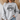 A woman wearing a light heather gray crewneck sweatshirt with a black graphic print that reads 'HIGHWAY JESUS TO HEAVEN'.