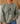 A person wearing an olive green crewneck sweatshirt with a dark green graphic of a frog riding a bicycle and the text 'Be Humble Be Kind Leave your worries BEHIND'.
