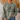 A person wearing an olive green crewneck sweatshirt with a dark green graphic of a frog riding a bicycle and the text 'Be Humble Be Kind Leave your worries BEHIND'.
