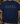 A navy blue short-sleeve t-shirt laid flat on a rustic wooden surface, featuring a hunting-themed graphic with deer, antlers, a duck, a bird, and a deer head, above the words 'HUNTING SEASON' in white. Camouflage hat, boots, binoculars, and antlers surround the shirt as styled props.