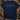 A navy blue short-sleeve t-shirt laid flat on a rustic wooden surface, featuring a hunting-themed graphic with deer, antlers, a duck, a bird, and a deer head, above the words 'HUNTING SEASON' in white. Camouflage hat, boots, binoculars, and antlers surround the shirt as styled props.