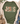 An olive green graphic t-shirt styled in a flat lay with a beige knit cardigan, blue jeans, brown suede boots, and pinecones. The t-shirt features a distressed graphic reading 'JESUS IS the reason' with a rustic holiday theme.