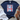 Navy blue t-shirt with 'Free Freedom Big' graphic design on a wooden surface with white shorts and brown sandals.