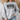 A woman wearing a light gray crewneck sweatshirt with a black graphic print that reads 'MADE for more' and 'EPHESIANS 2:10'.