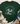 A dark green short-sleeve graphic T-shirt laid flat on a whitewashed wood surface, styled with a knit blanket, eucalyptus leaves, blue jeans, and beige ankle boots. The shirt has a large grayscale nativity scene print on the front.