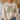 A person wearing a cream-colored crewneck sweatshirt with a detailed graphic of mallards and the Bible verse Philippians 4:4 on the front, set against a cozy indoor background.
