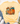 A pale yellow short-sleeve T-shirt laid flat on a white wood surface, styled with blue jeans, white sneakers, a straw hat, and eucalyptus. The shirt has a large autumn pumpkin graphic in orange, teal, brown, purple, and green tones on the front.