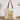 A cream canvas tote bag with brown shoulder straps stands on a wooden surface against a white wall. The front of the bag has a colorful autumn graphic with the text 'HEY THERE PUMPKIN' and an illustration of pumpkins, flowers, and leaves on a light blue background.