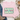 A folded light pink crewneck sweatshirt with a retro-style graphic reading 'SAVED BY GRACE' in cream, teal, and pink, styled on a white wood background with jeans, a boot, a coffee mug, and flowers.