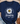 Navy blue t-shirt with a daisy graphic and text on a textured surface with jeans and sandals.
