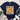 A navy blue short-sleeve t-shirt laid flat on a white wood background, featuring a large autumn turkey graphic with patterned feathers in orange, beige, and brown. The shirt is styled with a fringed cream throw, blue jeans, and white sneakers.