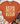 An orange short-sleeve t-shirt with a Thanksgiving turkey graphic, styled in a flat-lay arrangement with blue jeans, a knit blanket, and beige ankle boots on a white wood background.
