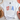 White t-shirt with 'USA' design on a white surface with shoes and decorative items.