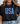 Person wearing a black t-shirt with 'USA' printed in blue stars, standing against a white wall.